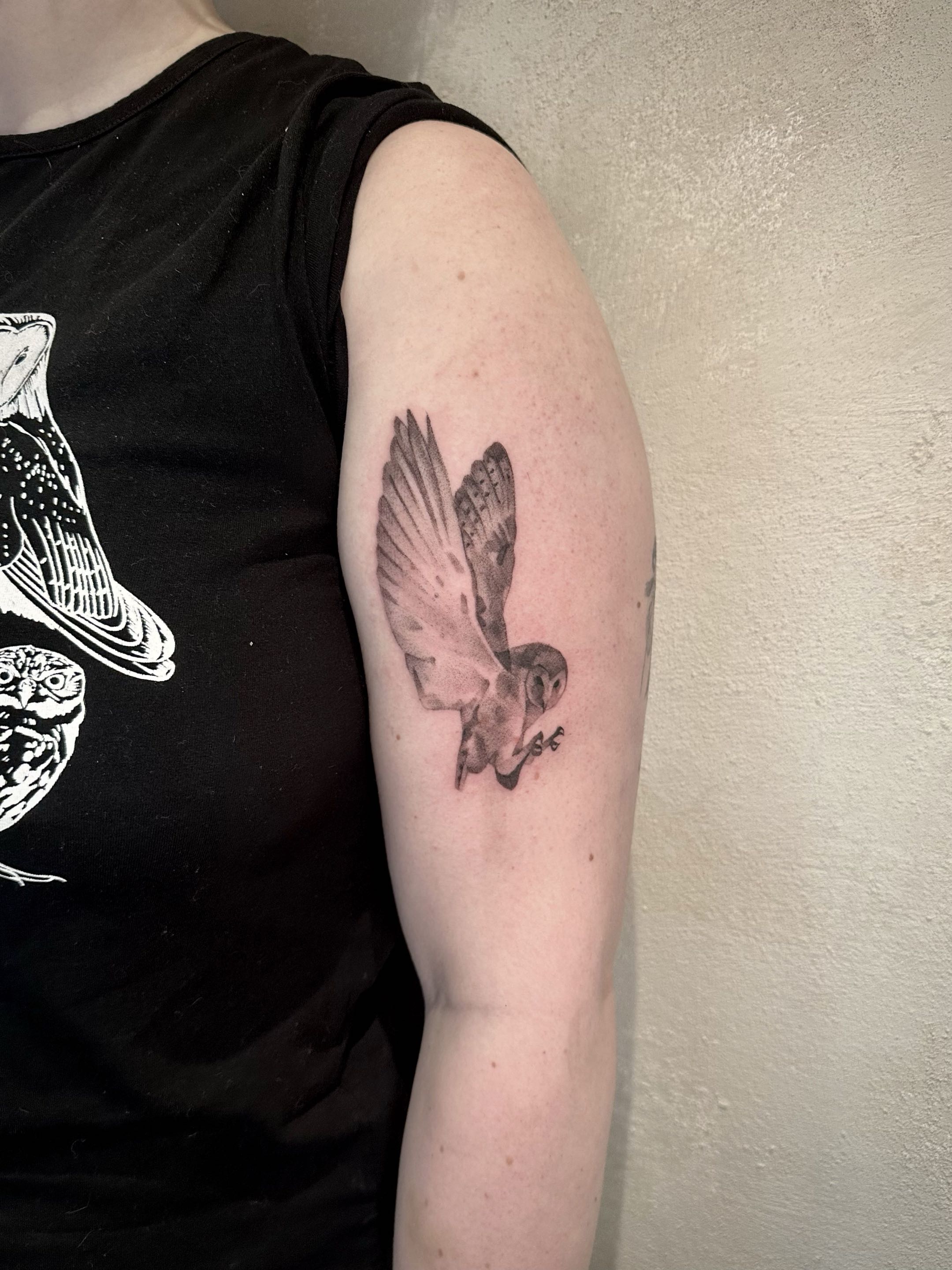 Black and grey fine art tattoo of a flying barn owl on a client's upper arm.