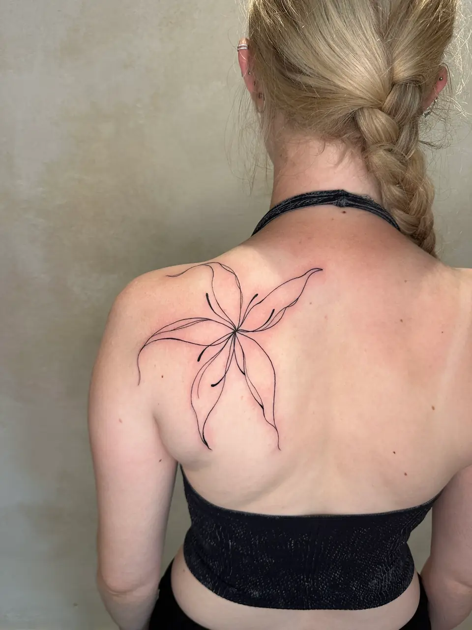 Large fine-line abstract flower with elongated petals across the shoulder blade.