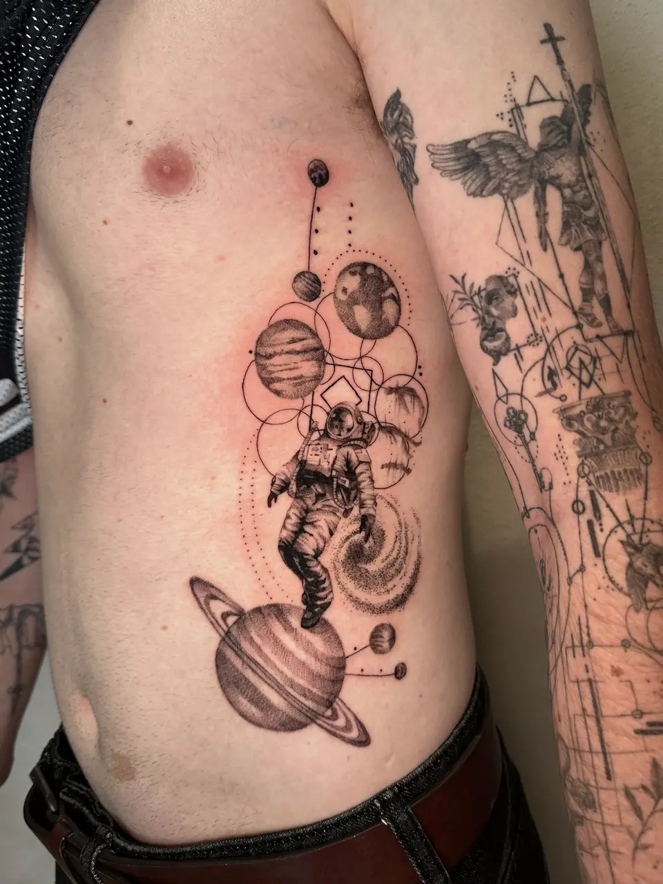 Shaded astronaut surrounded by planets, orbital lines and a ringed planet along the ribs.