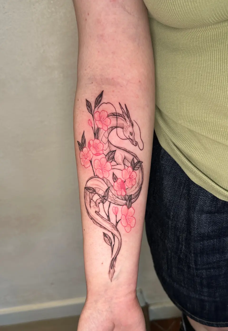 Slender outlined dragon winding among pink blossoms down the forearm.