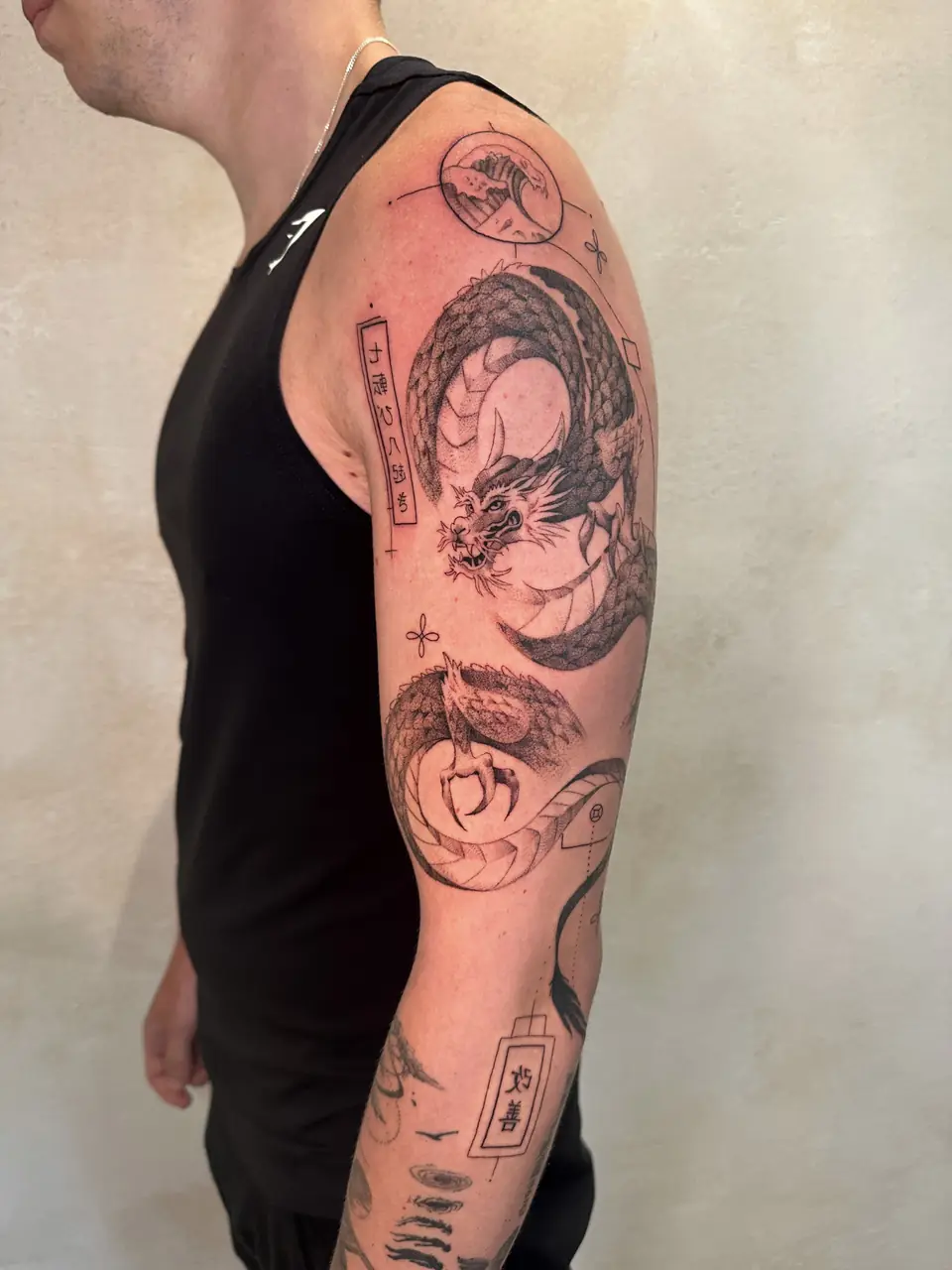 Black and grey coiled dragon with a wave vignette and geometric details along the arm.