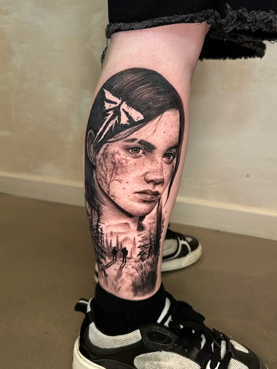 Black and grey Ellie portrait with the Firefly symbol and two figures in a forest scene on the calf.