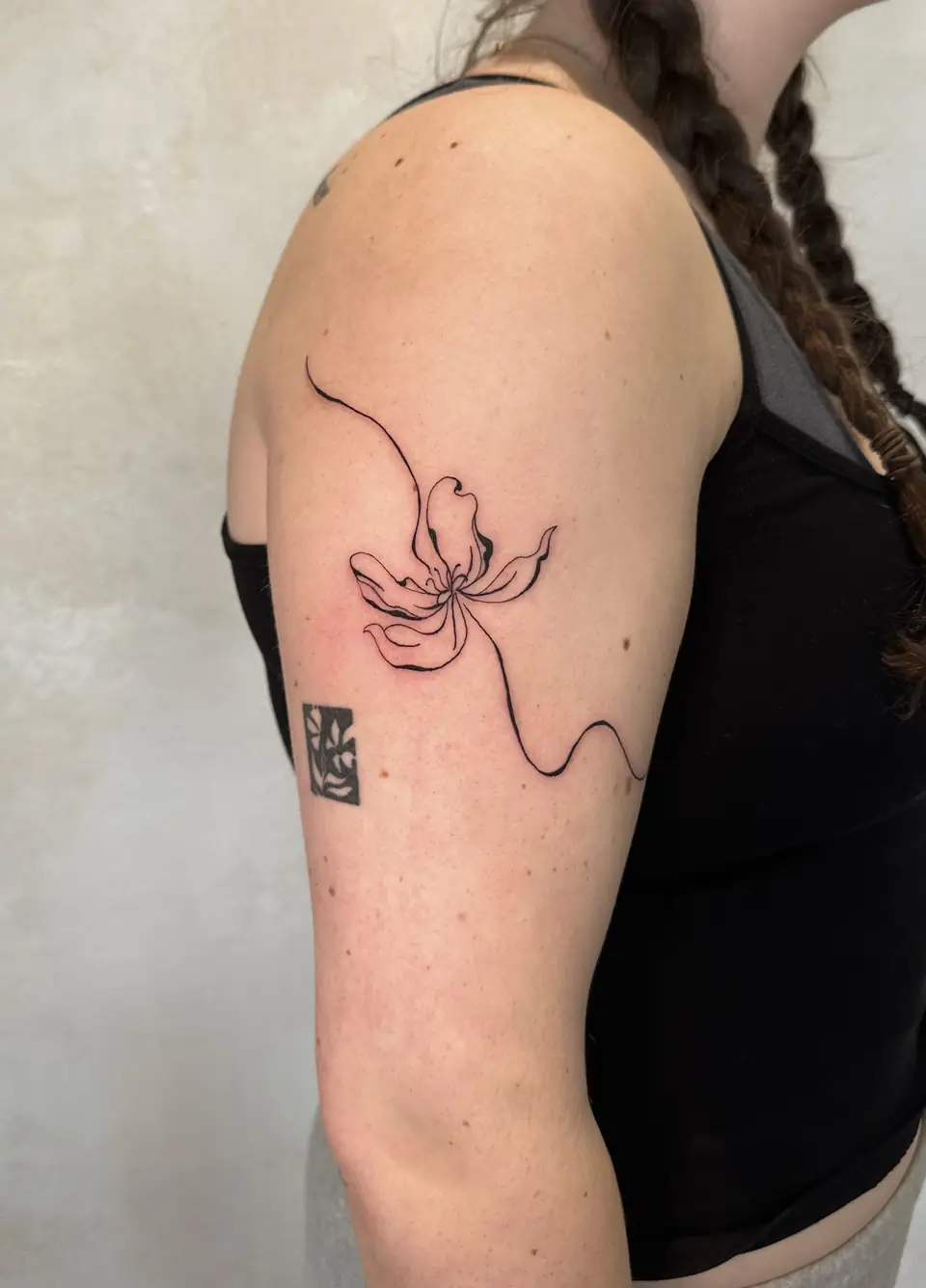 Fine-line abstract flower with a long flowing stem on the upper arm.