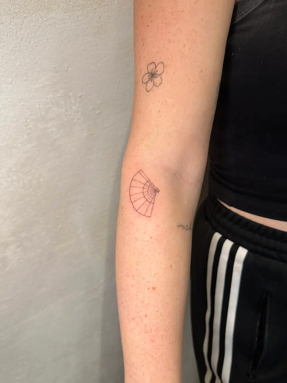 Delicate outline of an open folding hand fan near the elbow.