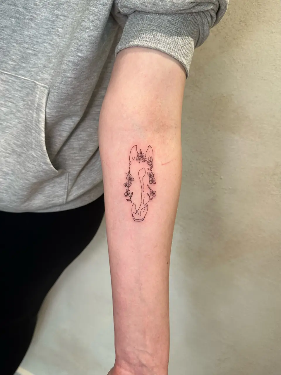 Fine-line horse head outlined with small flowers on the forearm.