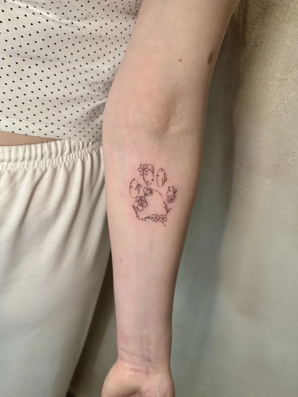 Paw-print outline formed from small flowers and leaves on the forearm.