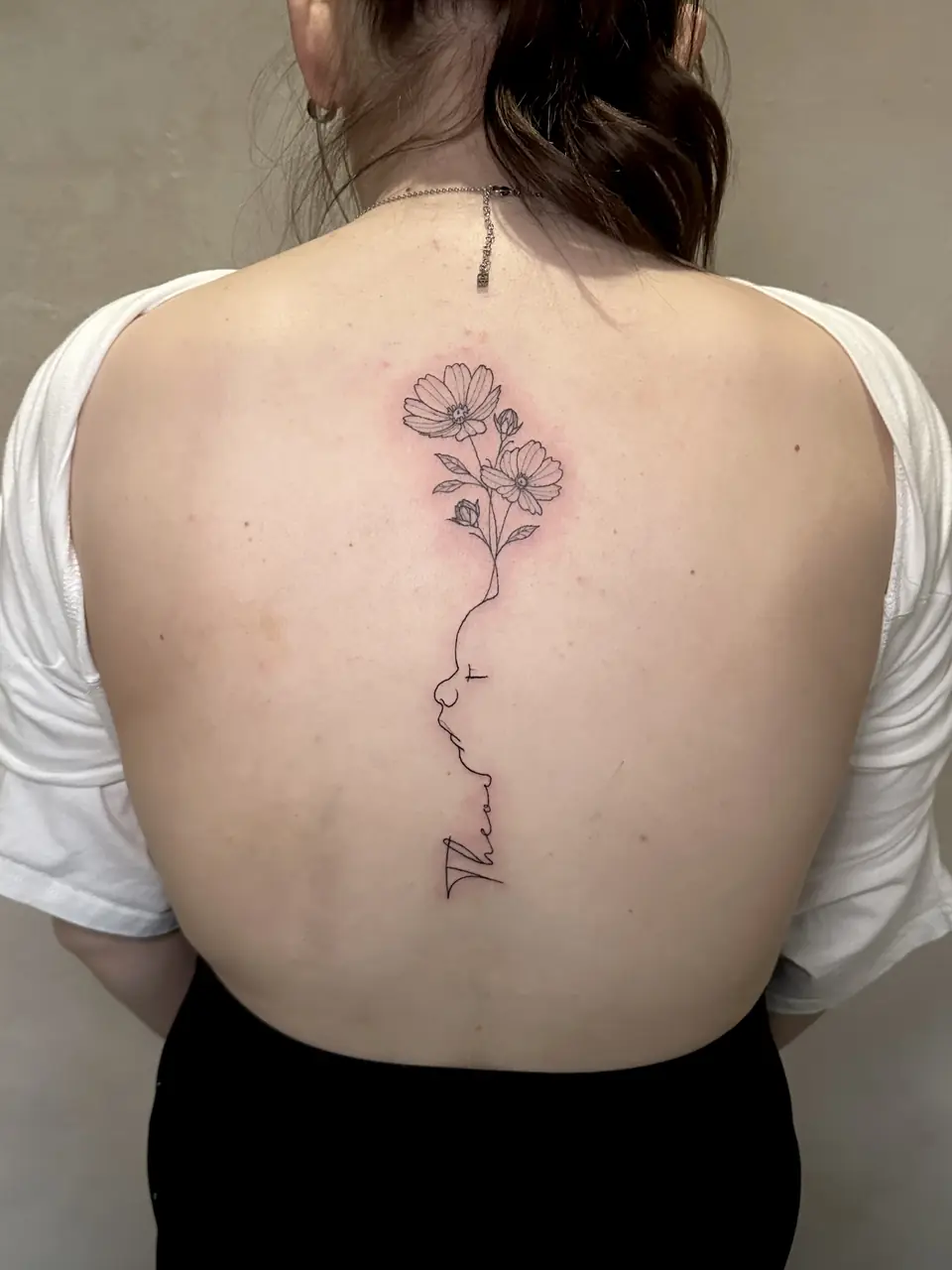 Fine-line flowers flowing into a face outline and script down the spine.