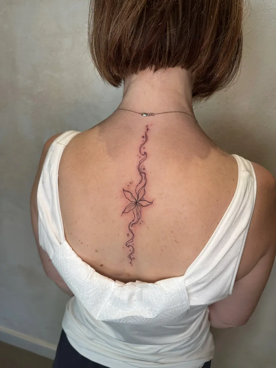 Fine-line flower woven into flowing ornamental lines down the upper spine.
