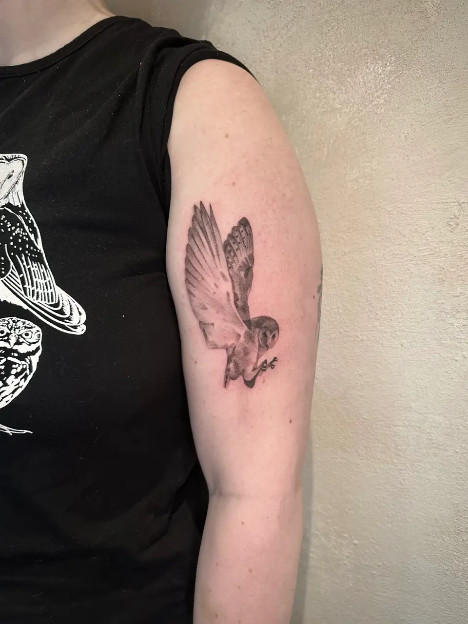 Black and grey barn owl in flight on the upper arm.