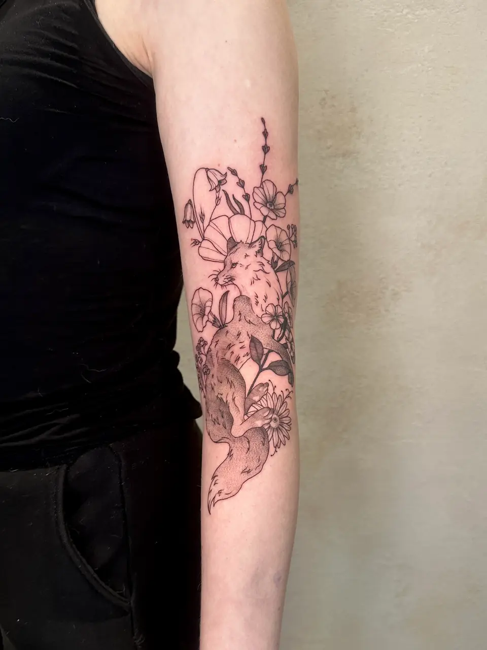 Illustrative fox surrounded by outlined wildflowers and leaves along the forearm.