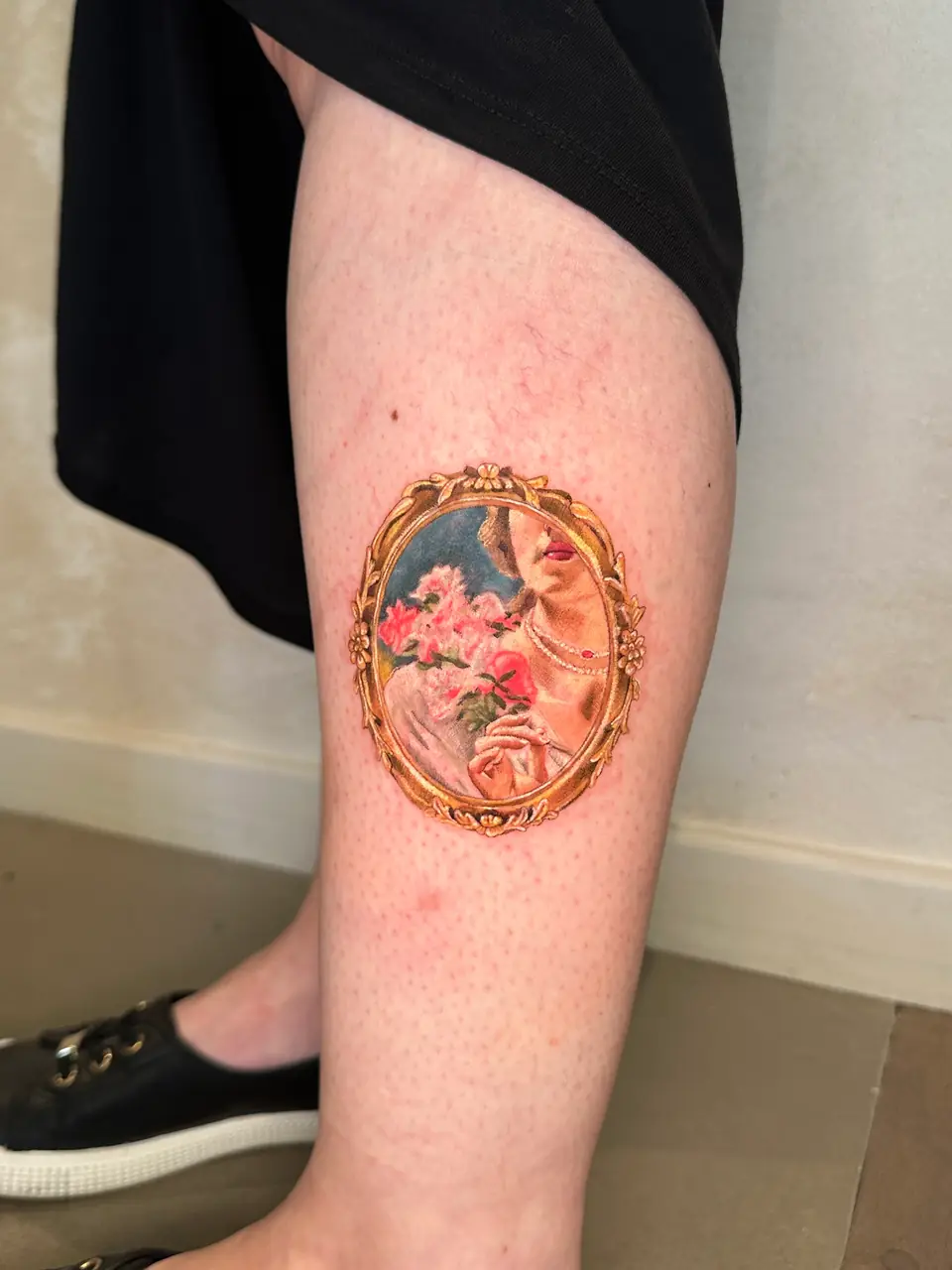 Colour portrait detail of a woman holding flowers inside an ornate gold oval frame on the calf.