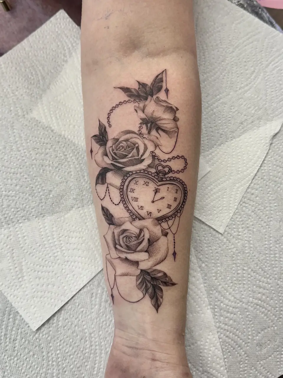 Heart-shaped pocket watch with Roman numerals, roses, a flower and a looping chain on the forearm.