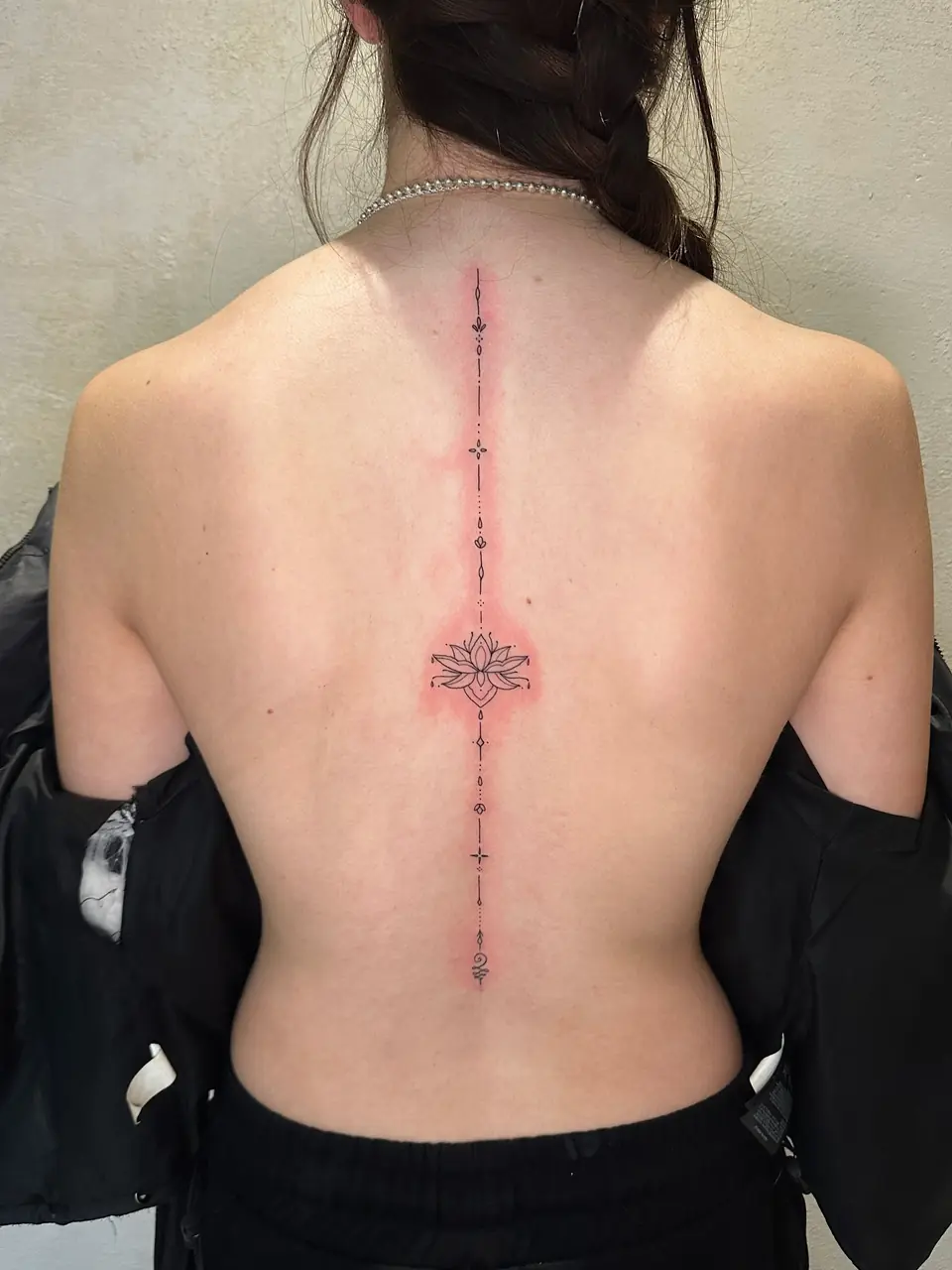 Fine-line lotus centred on a long vertical chain of ornamental marks along the spine.