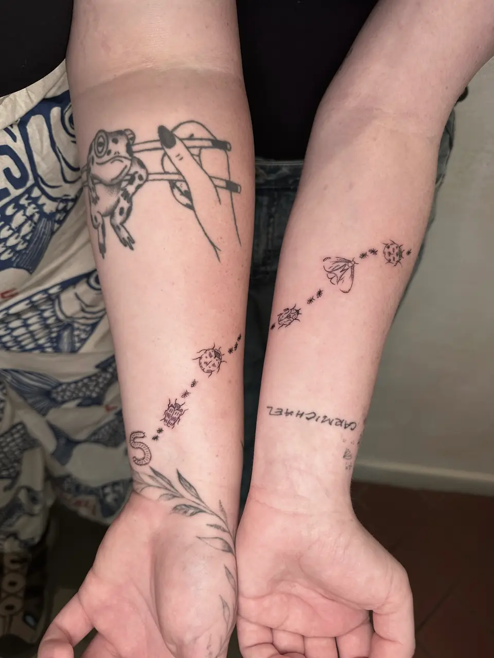 Matching chains of small insect motifs and star-like marks across two forearms.