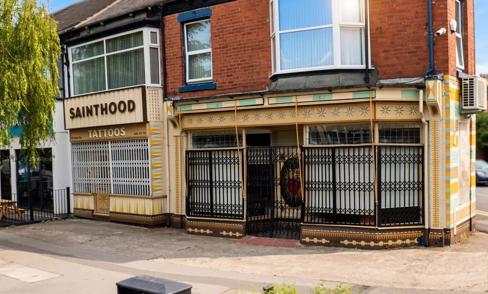 The Sainthood Tattoo shopfront on Princes Avenue in Hull, a corner unit with a yellow and teal tiled facade and a black metal grille.