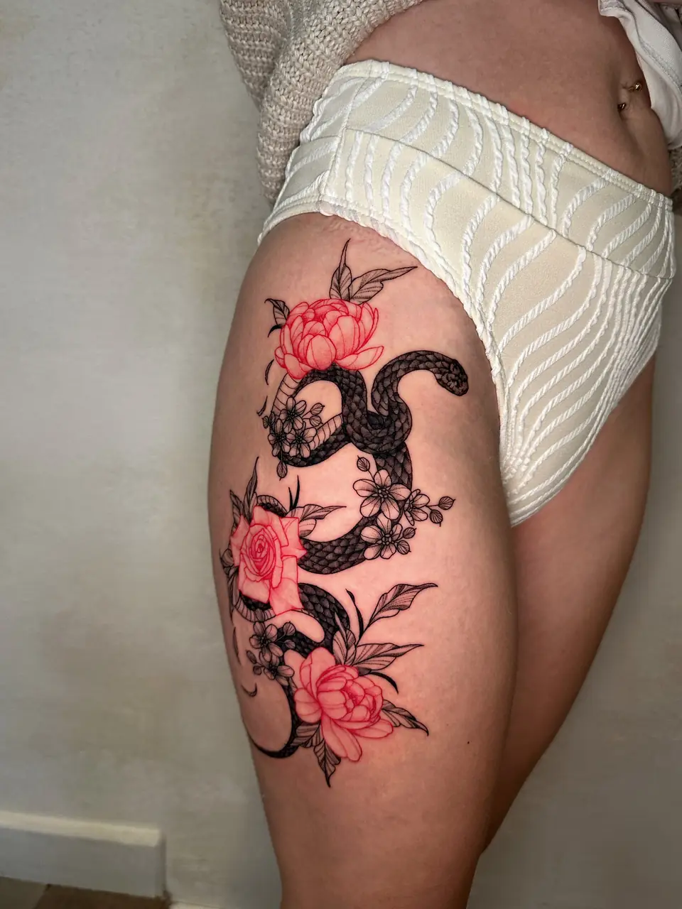 Black snake winding among red and black outlined flowers on the thigh.