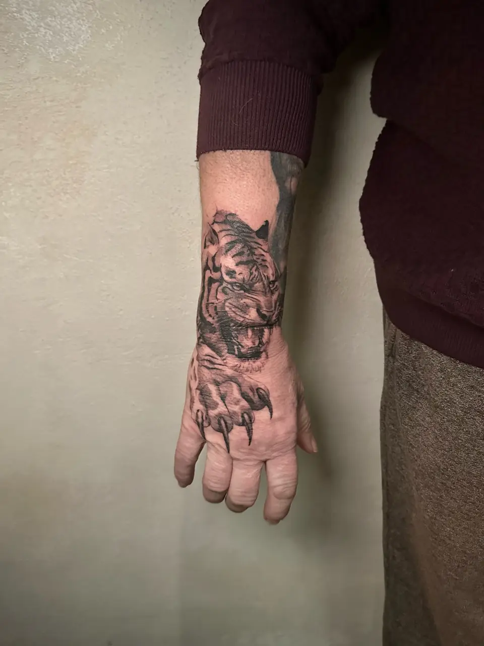 Black and grey tiger face across the wrist with a clawed paw on the back of the hand.