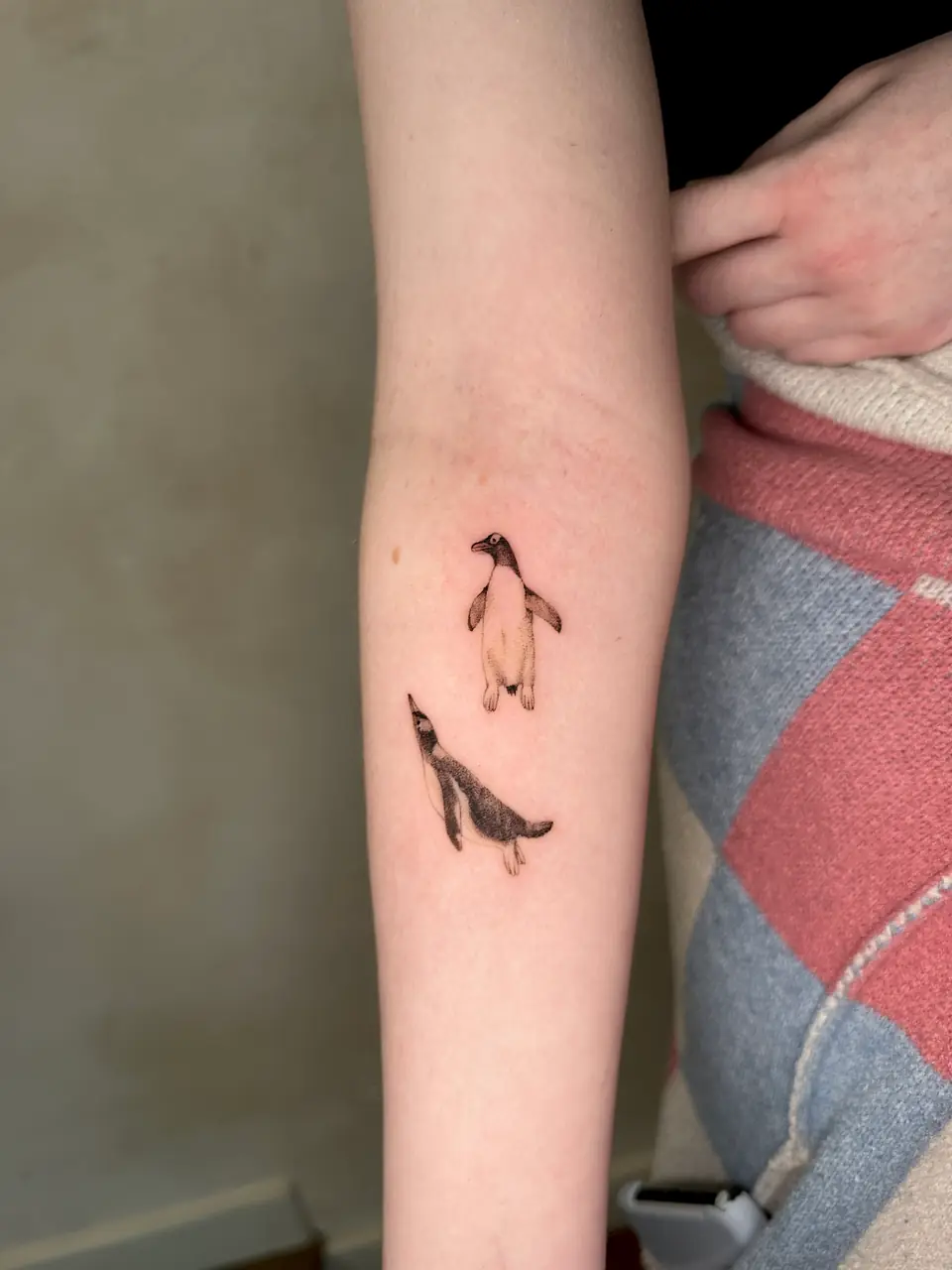 Two small black and grey penguins in different poses on the forearm.