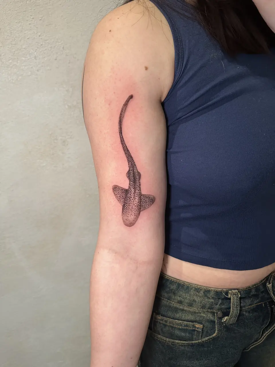 Spotted shark with a long curved tail and dotwork shading on the upper arm.